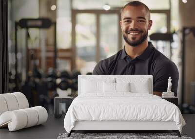 A high-definition photograph of a confident, smiling man in a modern gym, arms crossed Wall mural